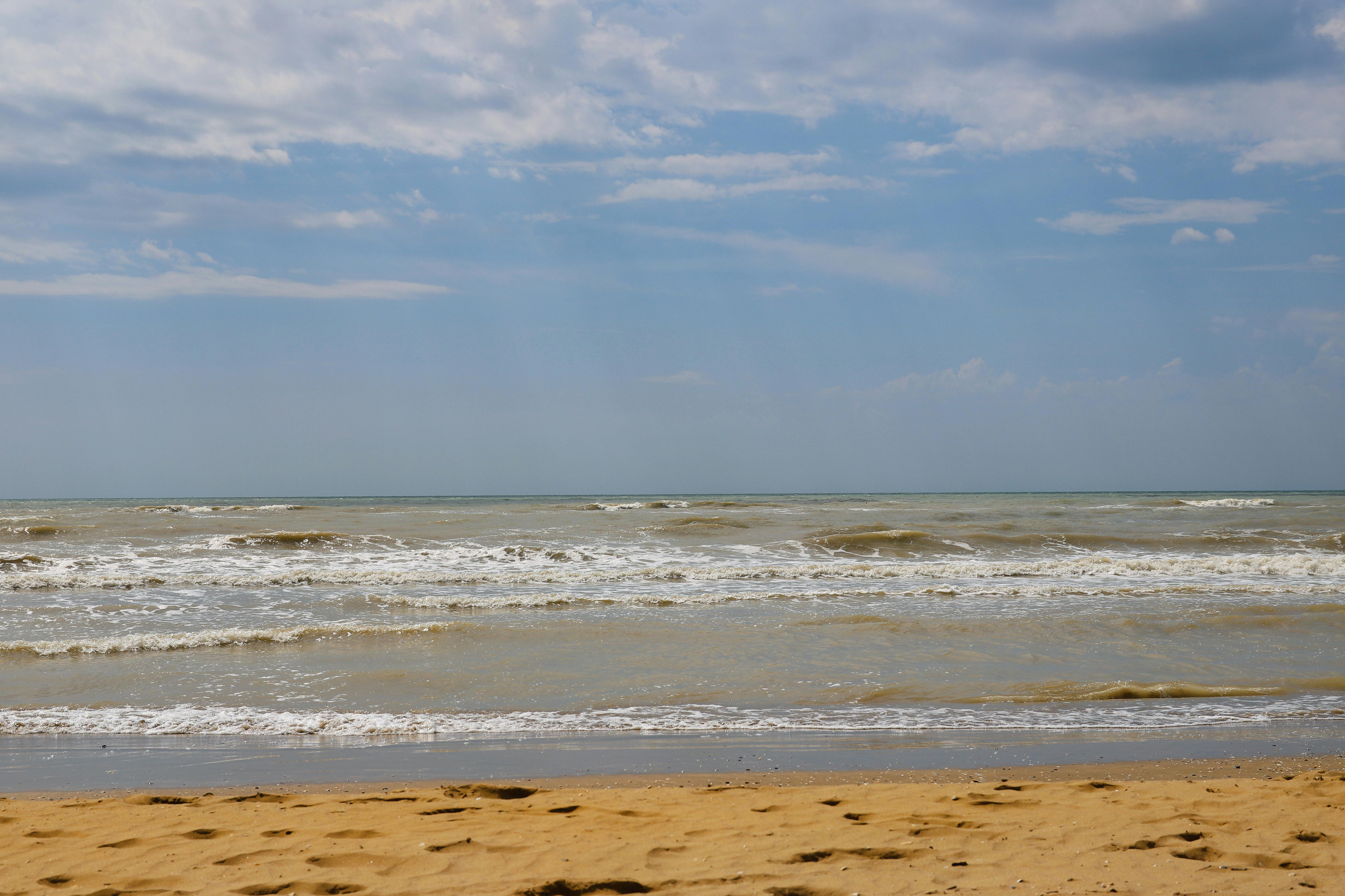 A serene beach scene with gentle waves under a partly cloudy blue sky in Veneto, Italy.