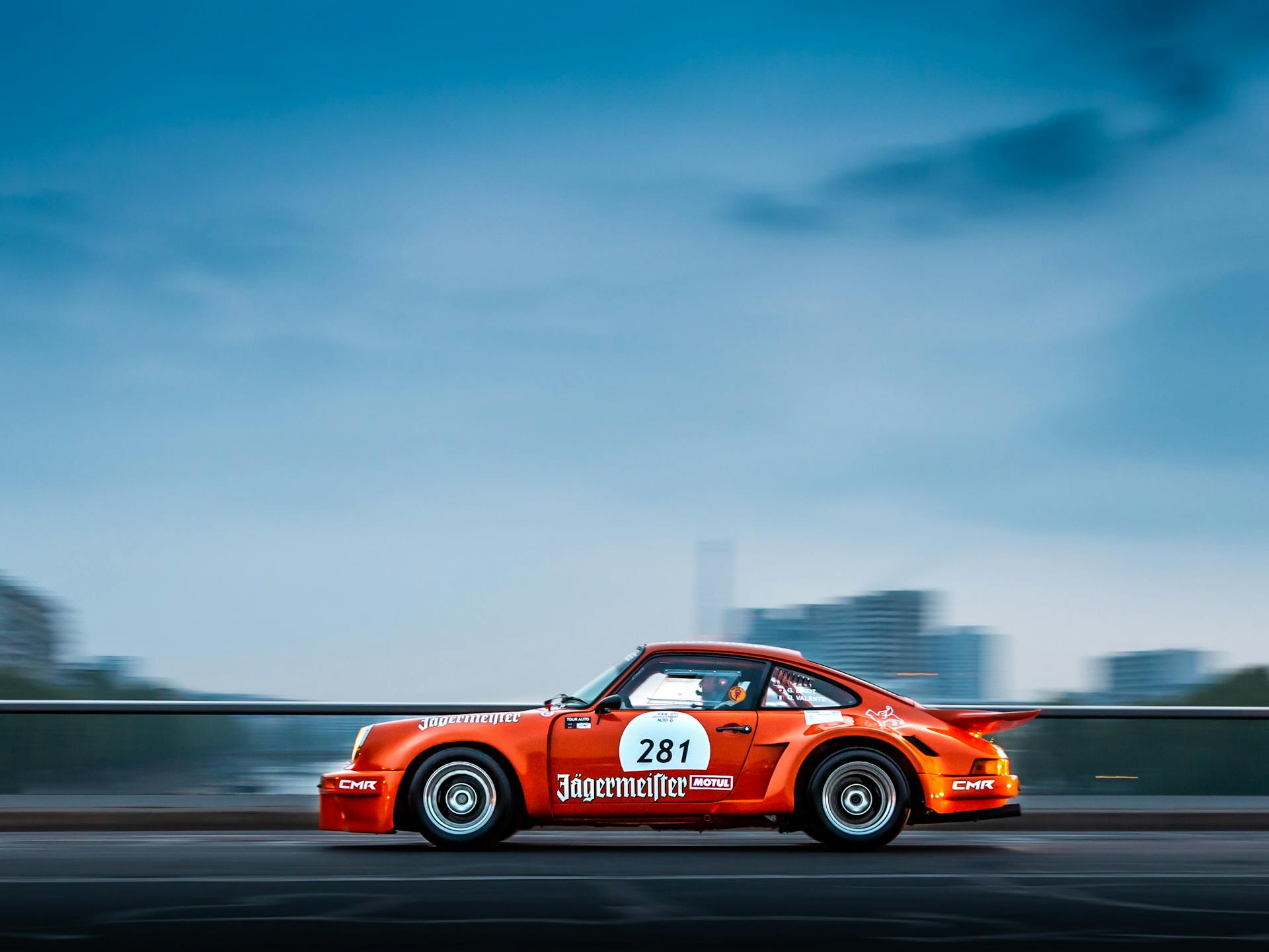 Dynamic shot of a vintage Porsche racing in Paris with blurred cityscape background.