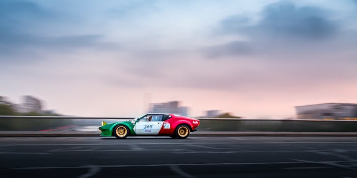 A classic car racing across a Paris bridge against a colorful sunset sky.