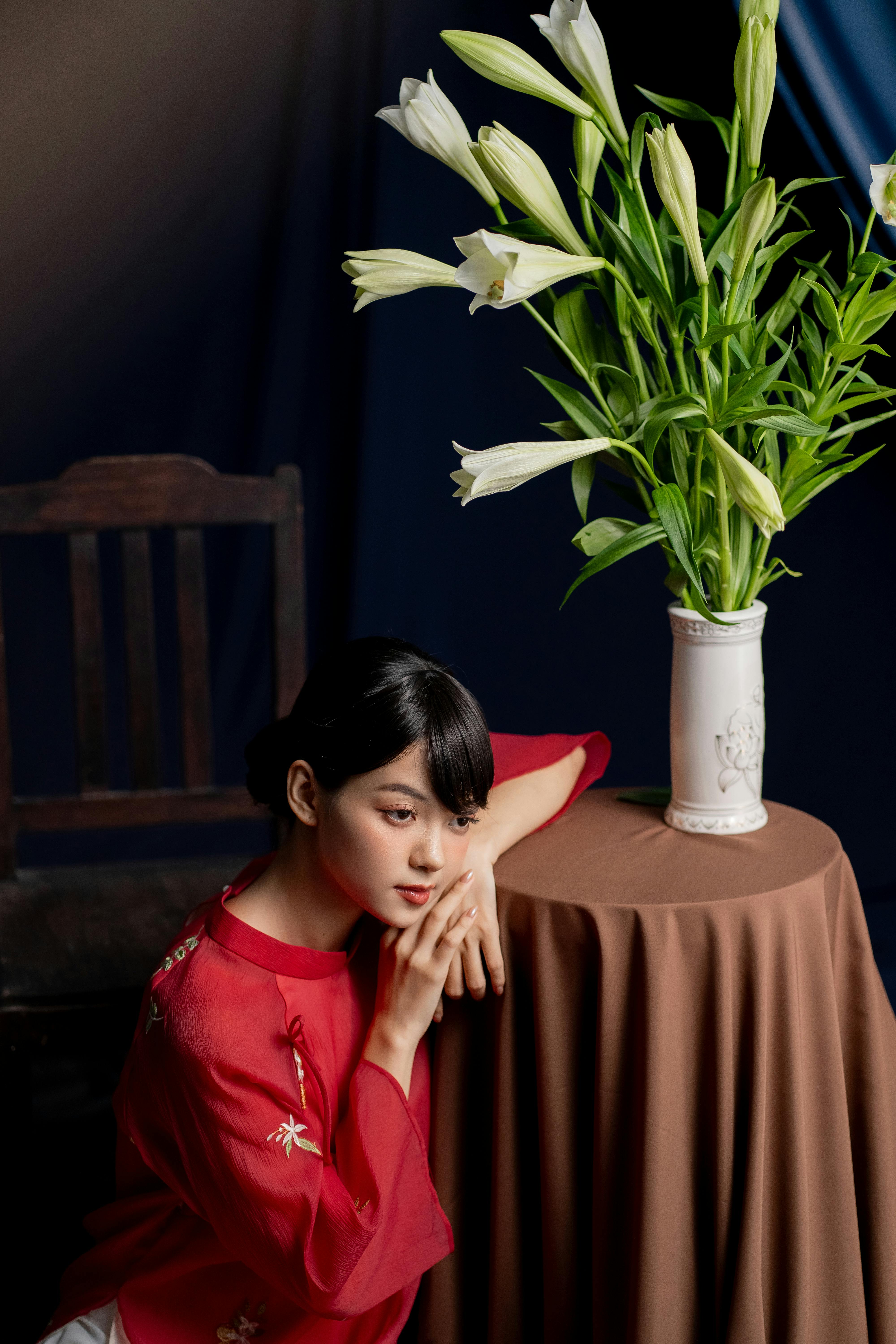 Woman in red with lilies on a classical indoor set, conveying elegance and calm.