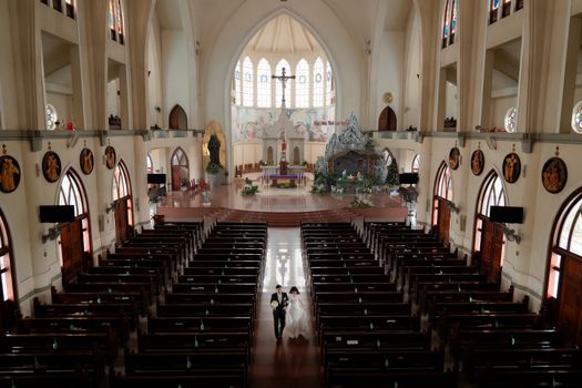 A bride and groom walk down the aisle in a beautiful Vietnamese church interior.