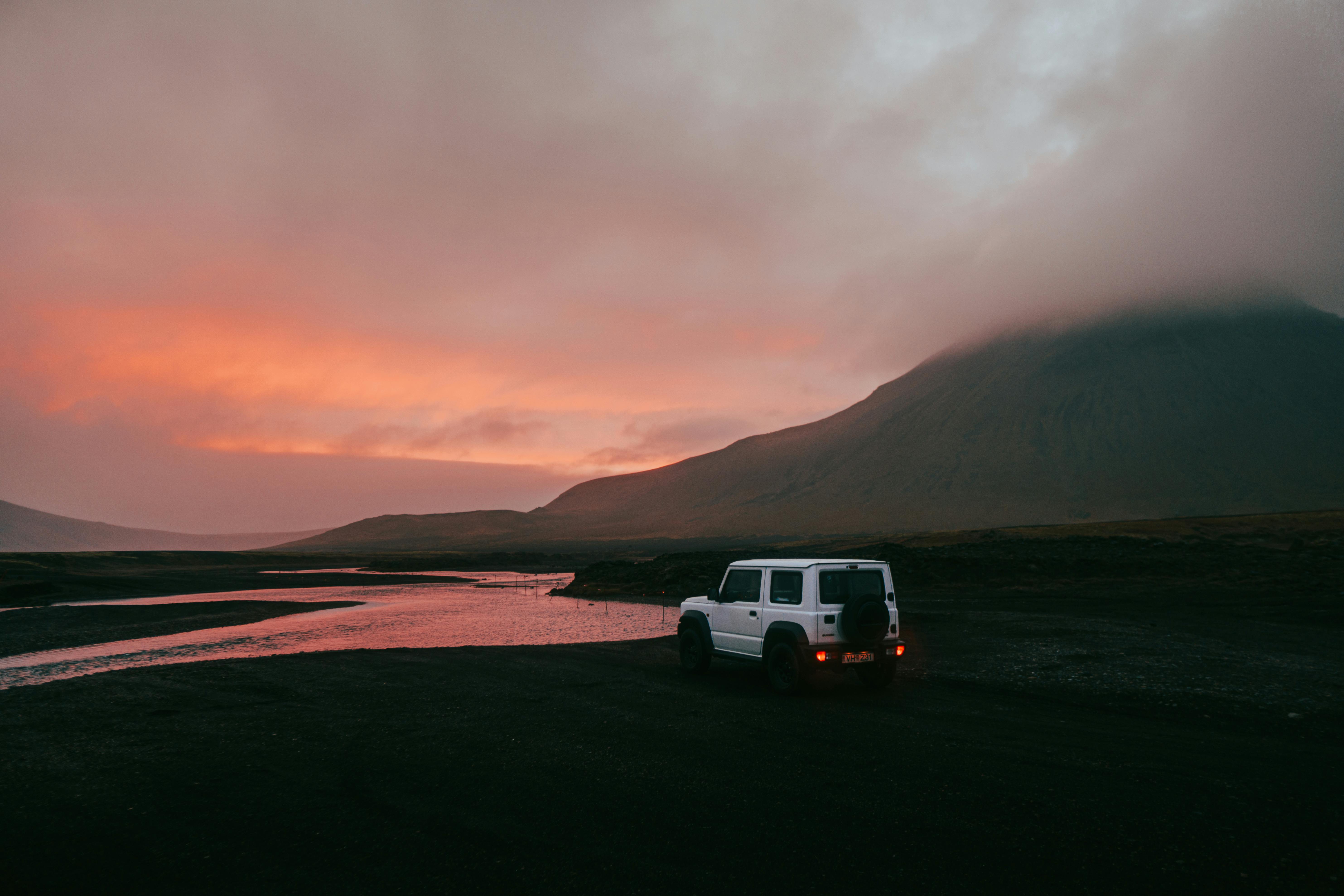White Suzuki Jimny facing a scenic river in Iceland during a vibrant sunset.