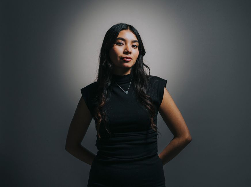 A confident young woman posing with studio lighting, creating a dramatic effect.