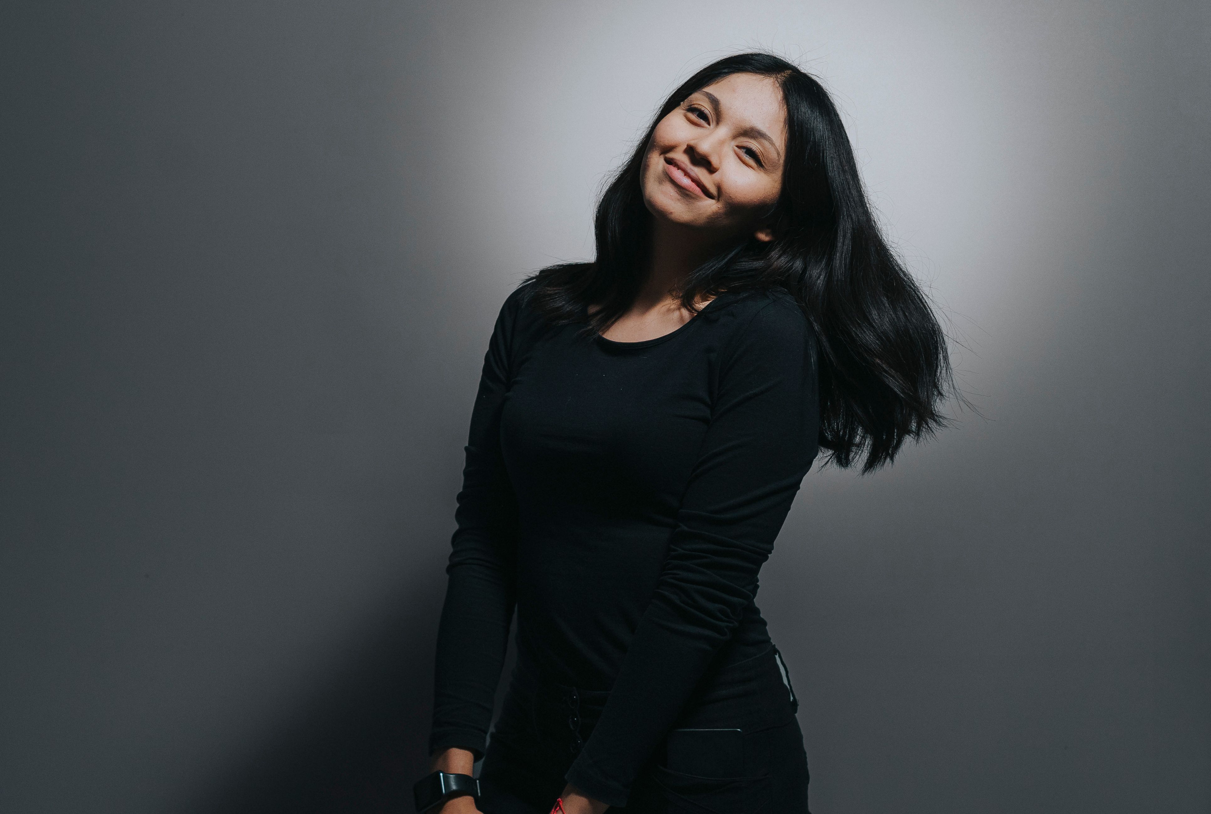 Portrait of a smiling woman in black attire, exuding warmth against a minimalist background.