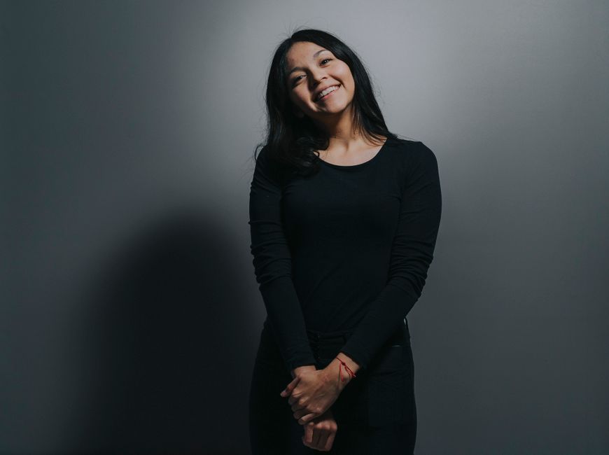 Simple portrait of a woman in black clothing smiling against a gray background.