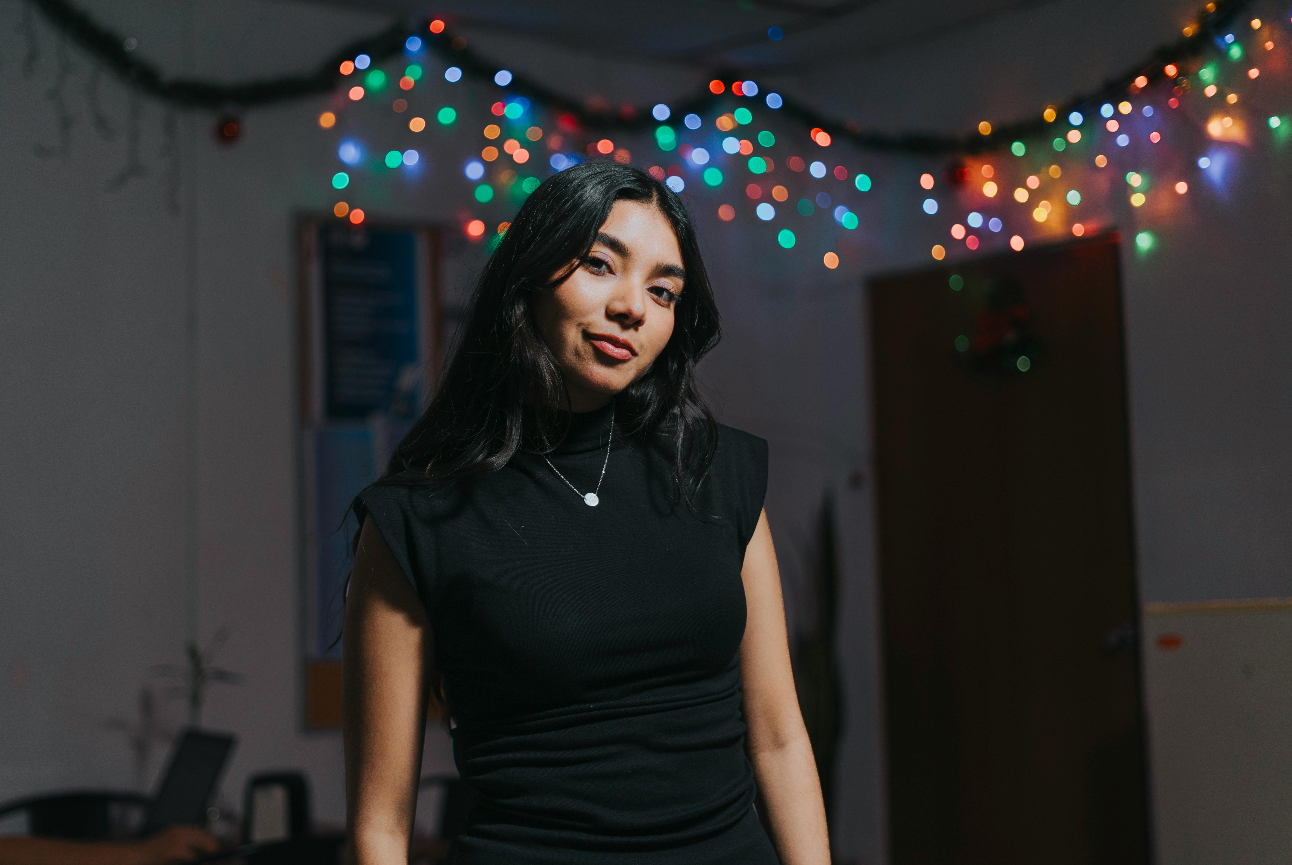 Kostenlos Eine selbstbewusste junge Frau steht im Innenbereich mit bunten Lichterketten im Hintergrund. Stock-Foto