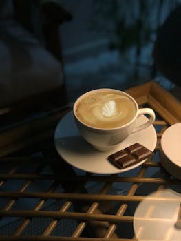 Warm cup of latte with latte art and chocolate on a glass table. Perfect for cozy, relaxing moments.