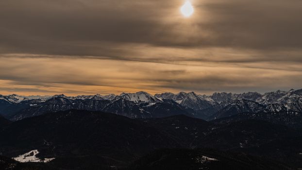 Panoramic view of the Bavarian Alps under a dramatic sunset sky in Kochel, Germany.