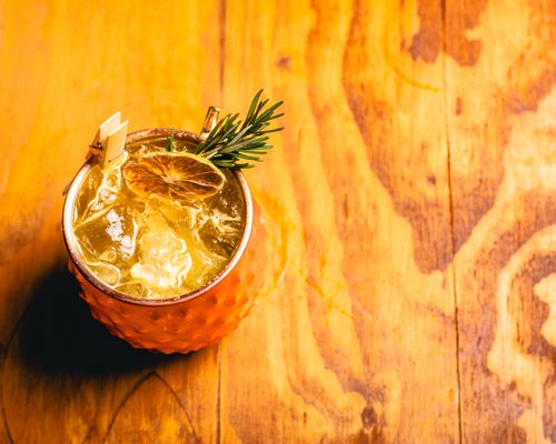 Free Copper mug with cocktail garnished with citrus slice and rosemary sprig on wooden table. Stock Photo