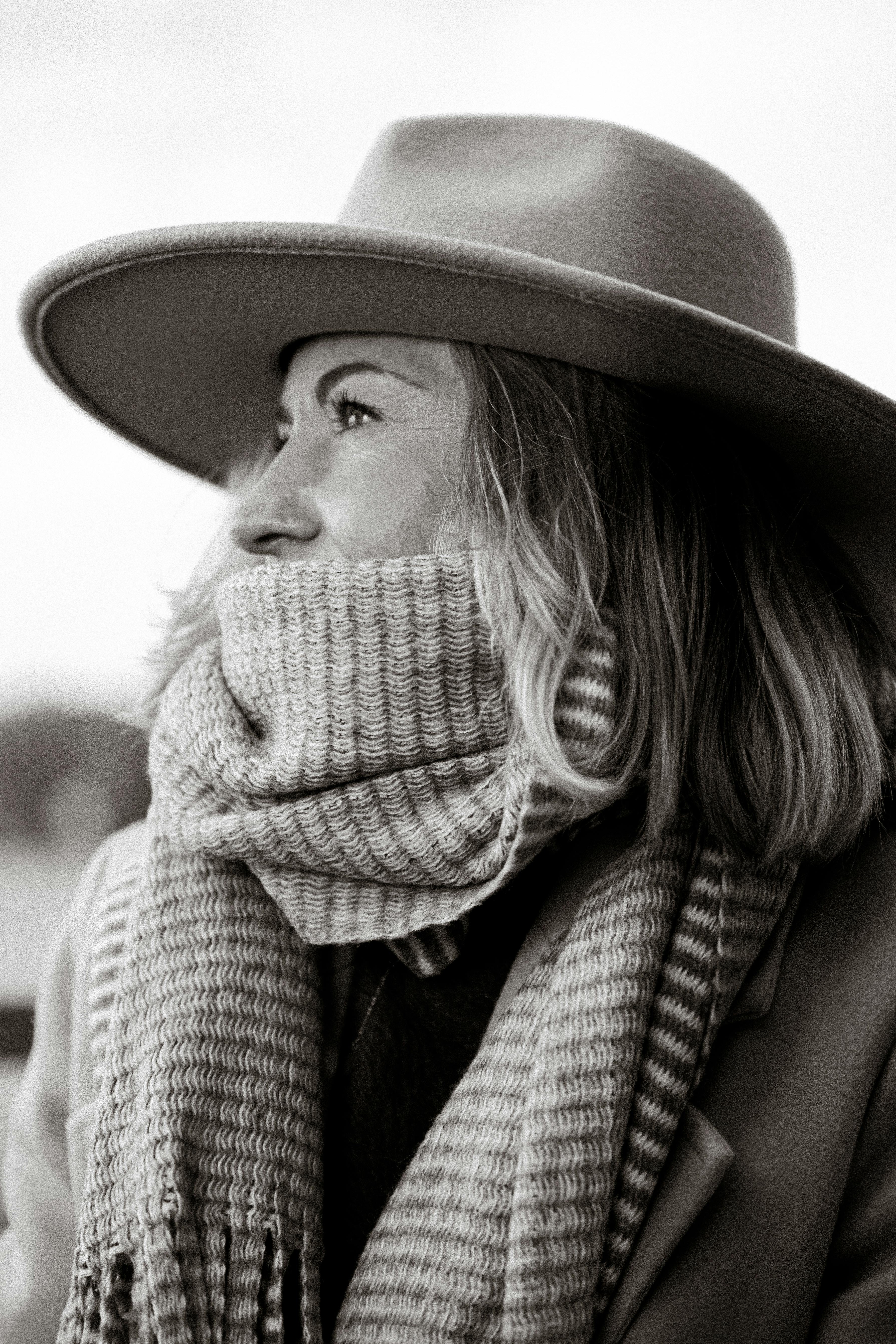Black and white portrait of a woman in a cozy scarf and hat, capturing a thoughtful winter moment.