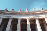 Majestic view of arched architectural columns with statues in Vatican City, under a clear blue sky.