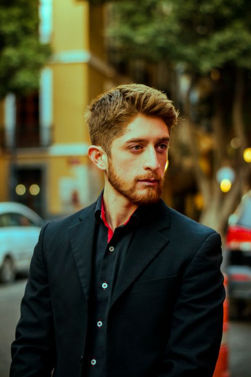 Free Young man in a suit on a city street, wearing a stylish blazer and thoughtful expression. Stock Photo