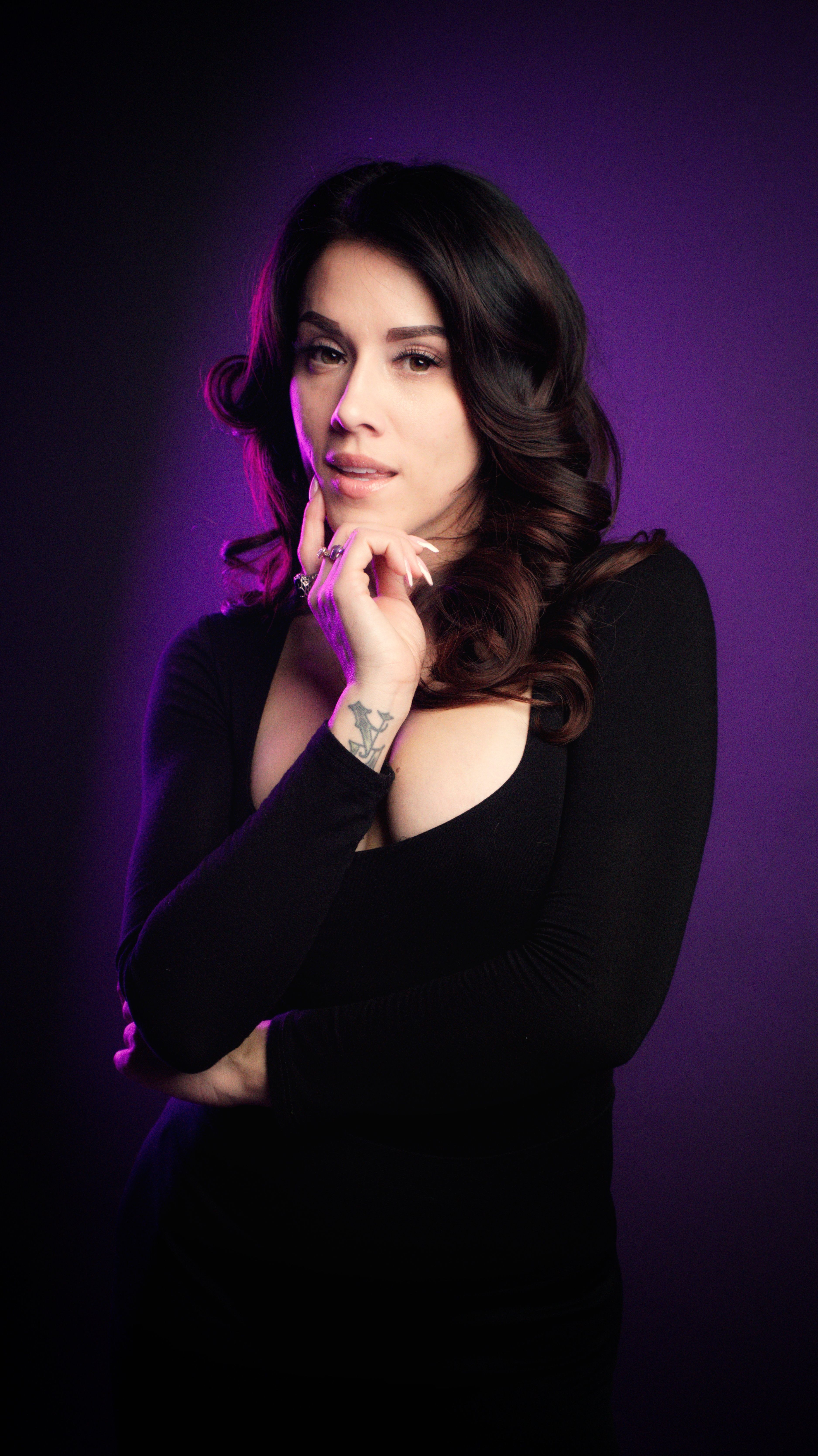 A captivating portrait of a woman in a black bodysuit on a purple backdrop, exuding elegance.