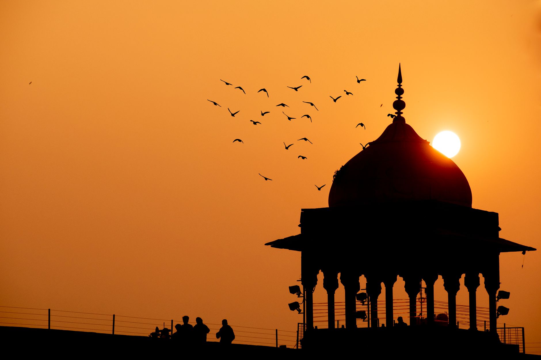 Silhouette view of Humayun's Tomb in Delhi at sunset, featuring birds in flight and rich orange hues.