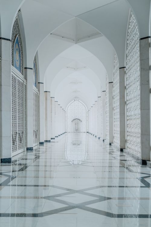 Free Beautifully designed arched hallway in a mosque featuring Islamic architectural details and marble flooring. Stock Photo