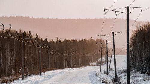 Free Snow-covered road with power lines in Ust-Kut, Russia during winter. Peaceful rural scene. Stock Photo