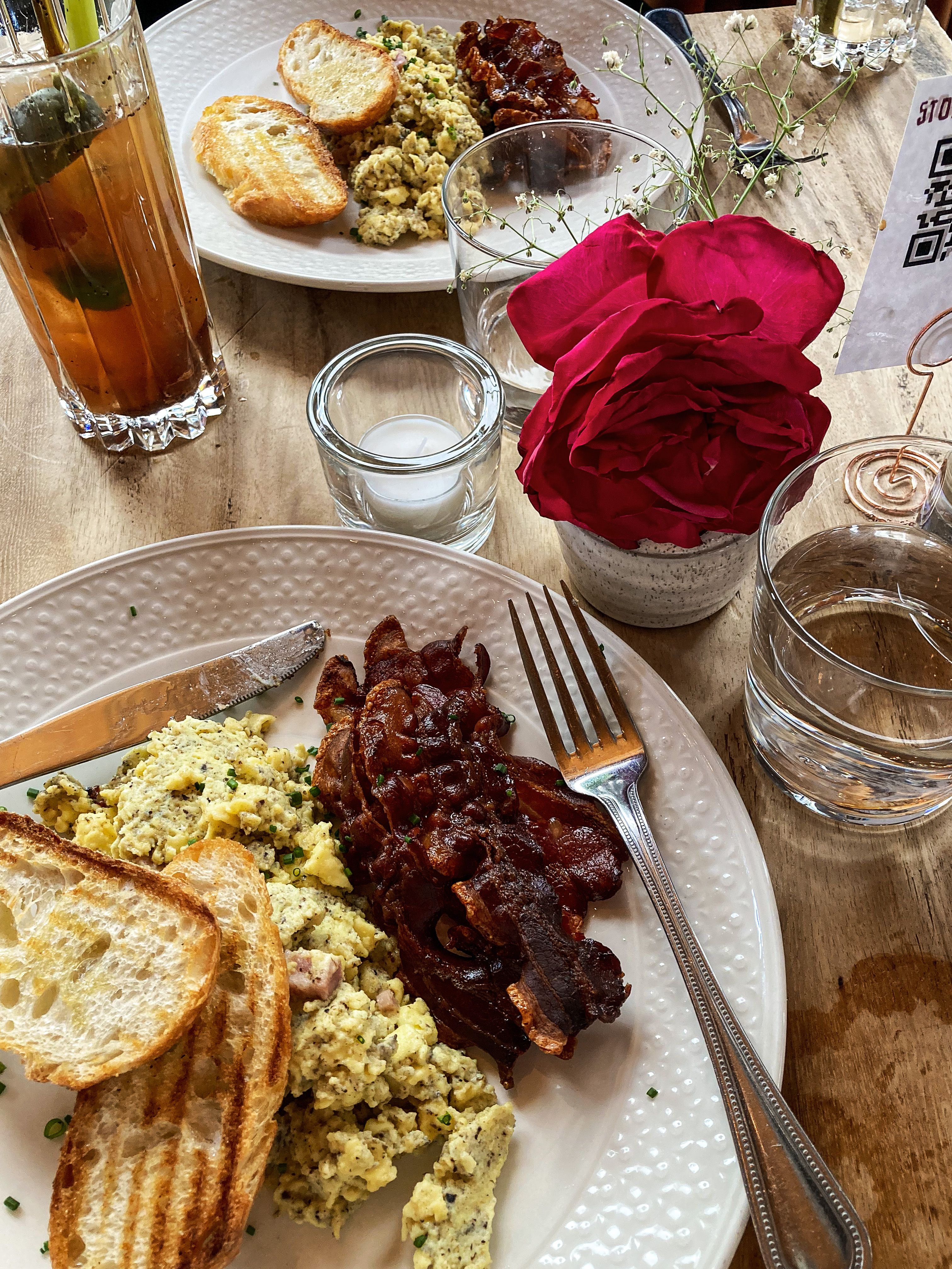 Scrumptious homemade brunch featuring scrambled eggs, bacon, toast, and a vibrant red rose.