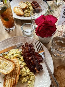 Scrumptious homemade brunch featuring scrambled eggs, bacon, toast, and a vibrant red rose.
