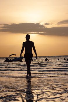 A person walking on a beach during sunset, with a boat in the water.
