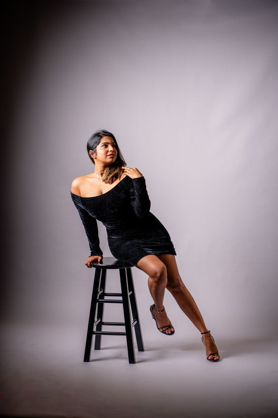 Woman in a black dress seated on a studio stool