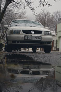 Old Volkswagen car reflected in a puddle on a snowy street, creating a moody urban scene.