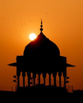 Silhouette of a pavilion in Delhi, India at sunset, casting a dramatic outline against an orange sky.