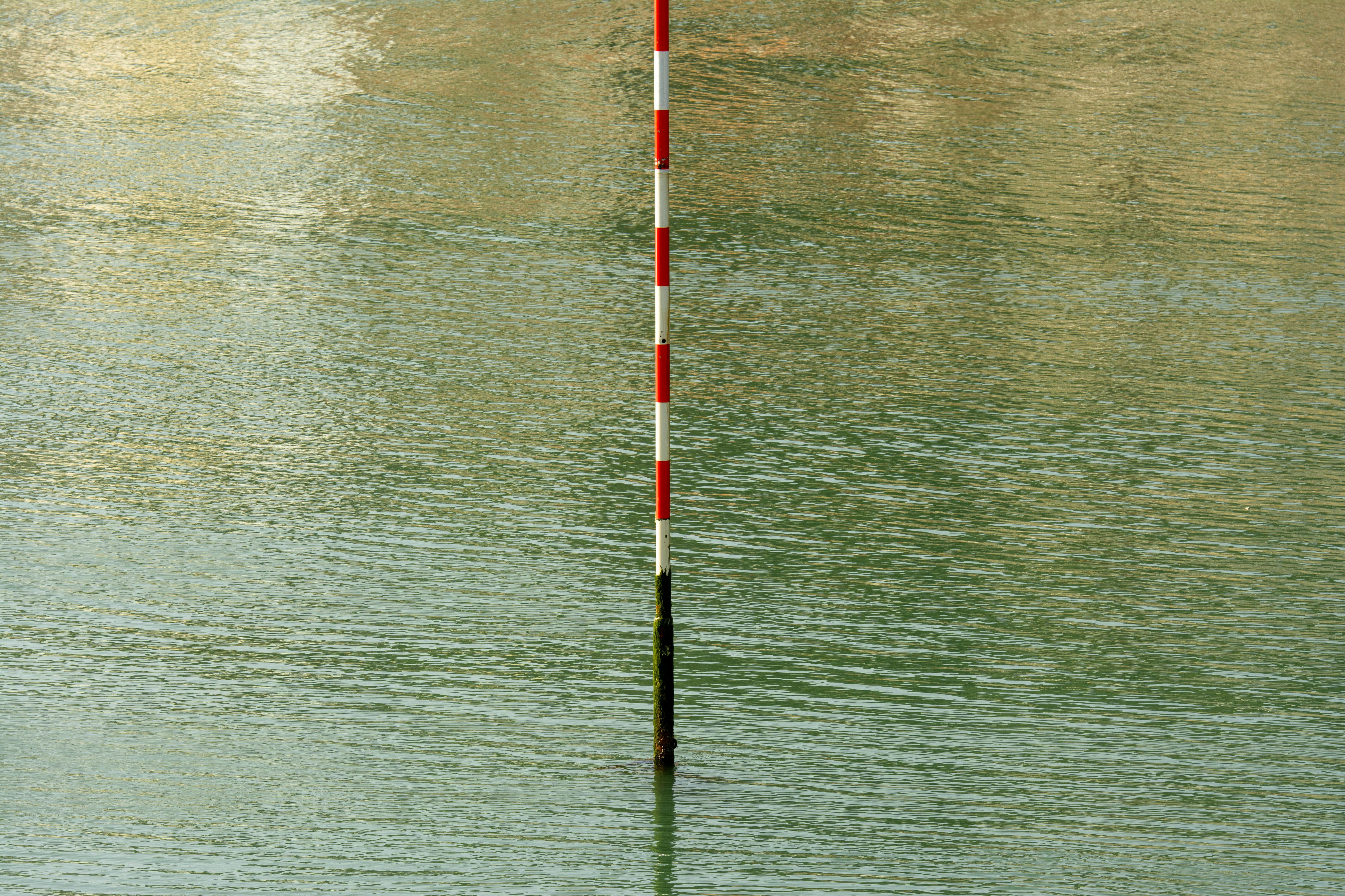 Gratis Un poste rojo y blanco se yergue en aguas tranquilas, reflejando quietud y mesura. Foto de stock