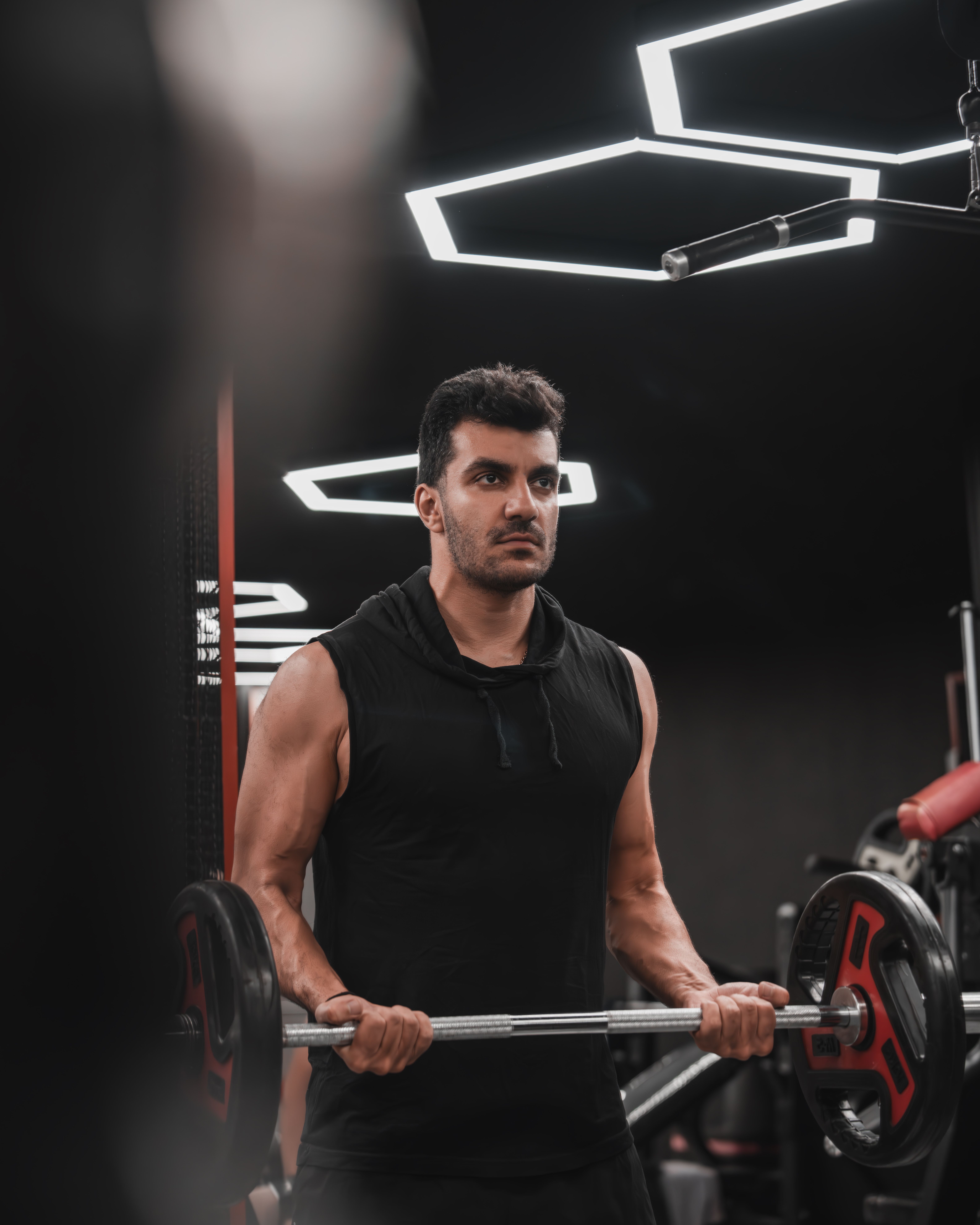 Determined man lifting weights in a stylish gym with geometric lighting.