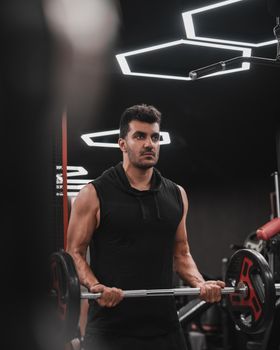 Determined man lifting weights in a stylish gym with geometric lighting.
