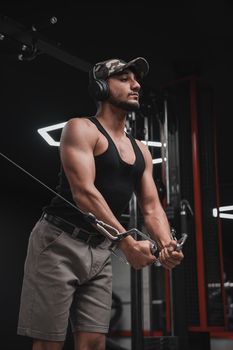 A man in a gym working out with a cable machine, wearing headphones.