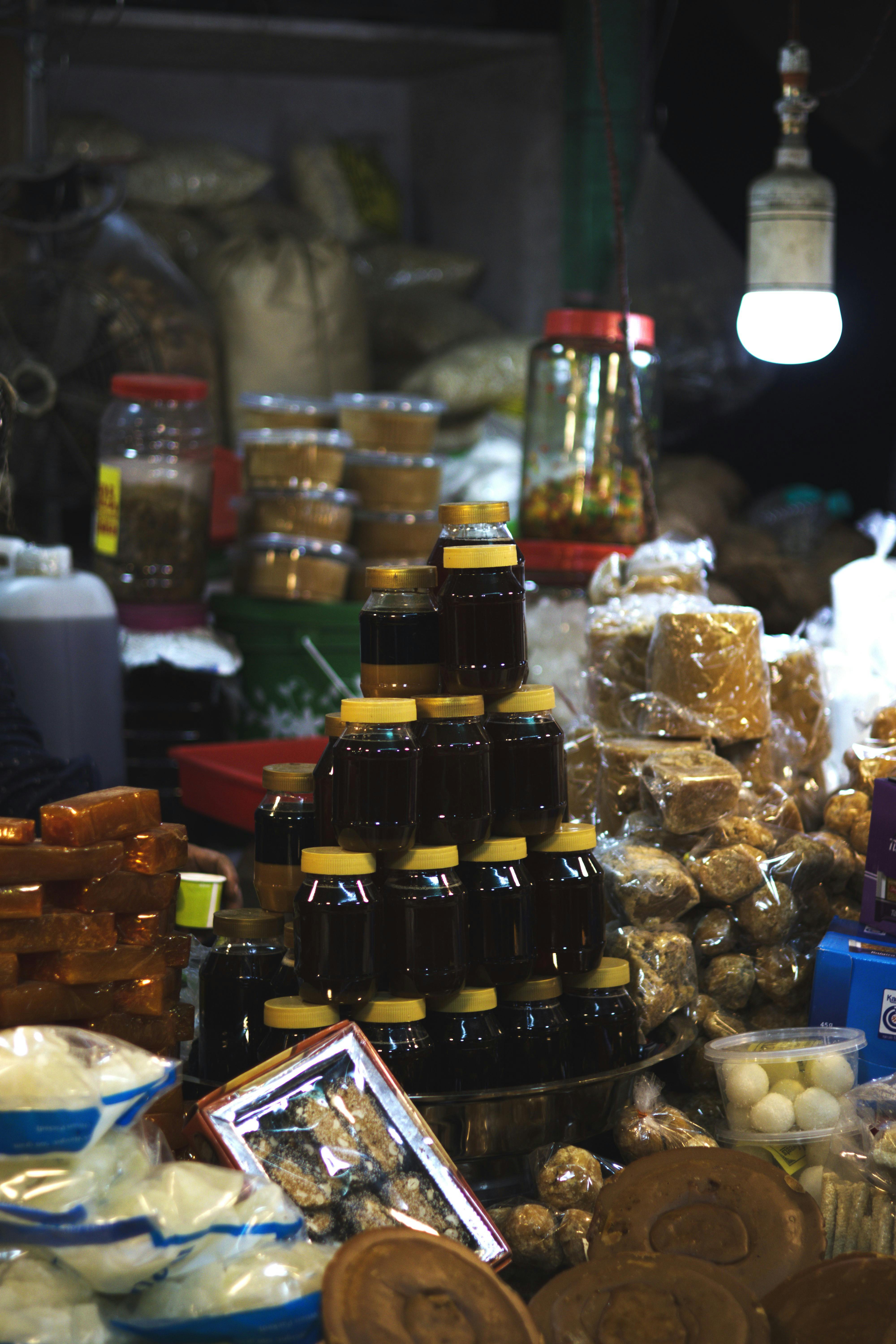 A vibrant market stall with stacked jars, spices, and edible goods under warm lighting.