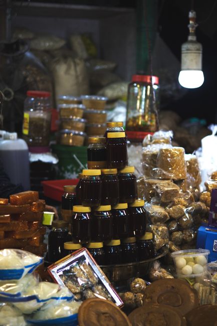 A vibrant market stall with stacked jars, spices, and edible goods under warm lighting.