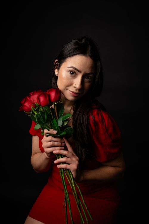 Free Portrait of a woman in a red dress holding a bouquet of red roses against a dark background. Stock Photo