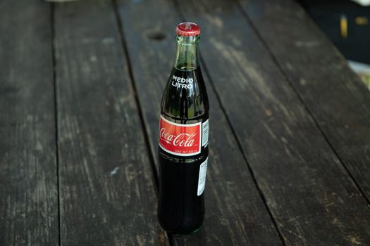 Een klassieke Coca-Cola-fles op een rustieke houten tafel buiten.