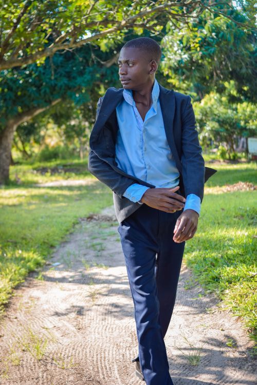 Free A man confidently walks outdoors in a stylish suit amidst a lush green background. Stock Photo