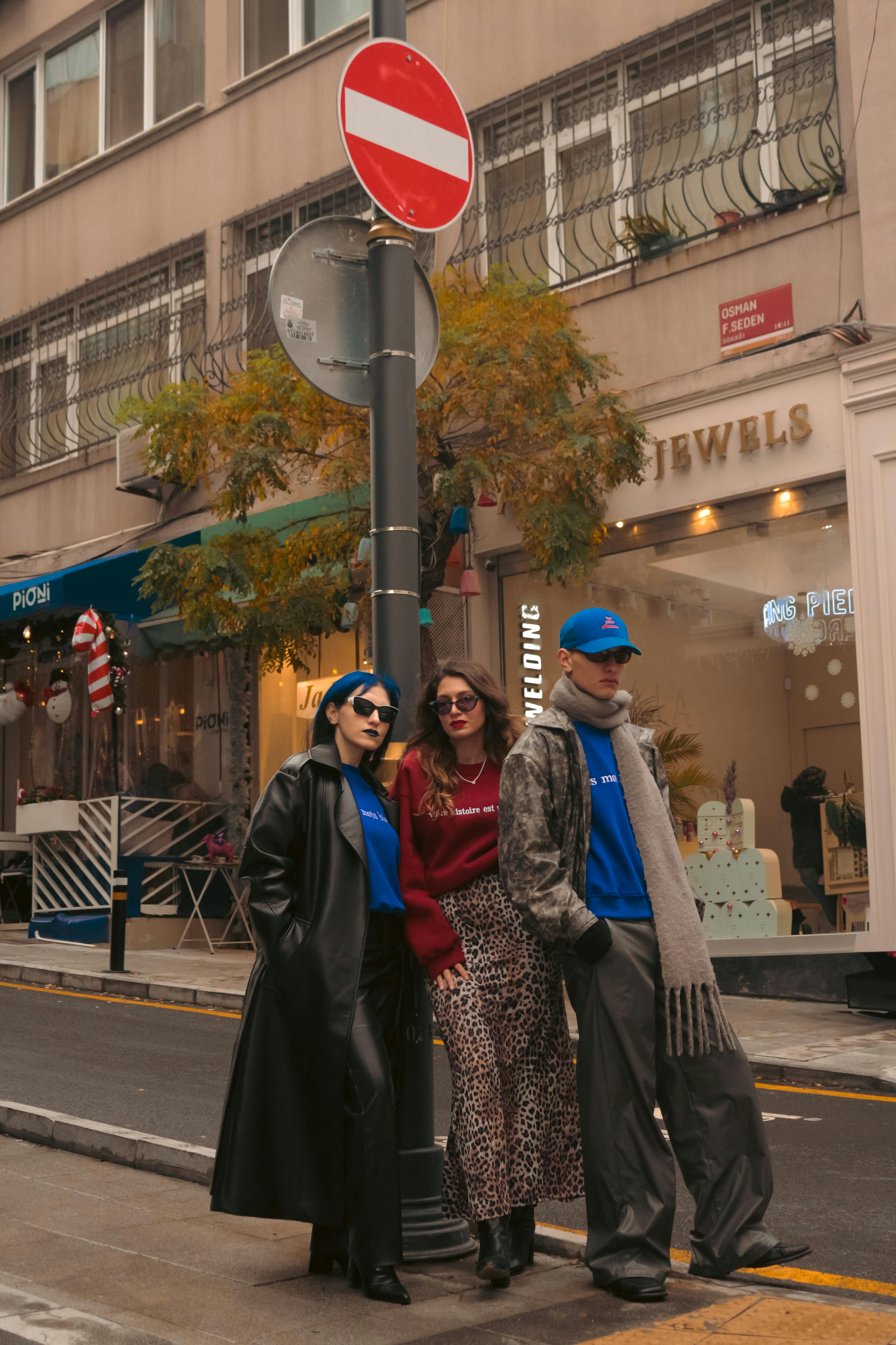 Three stylish adults pose on a city street showcasing modern urban fashion.