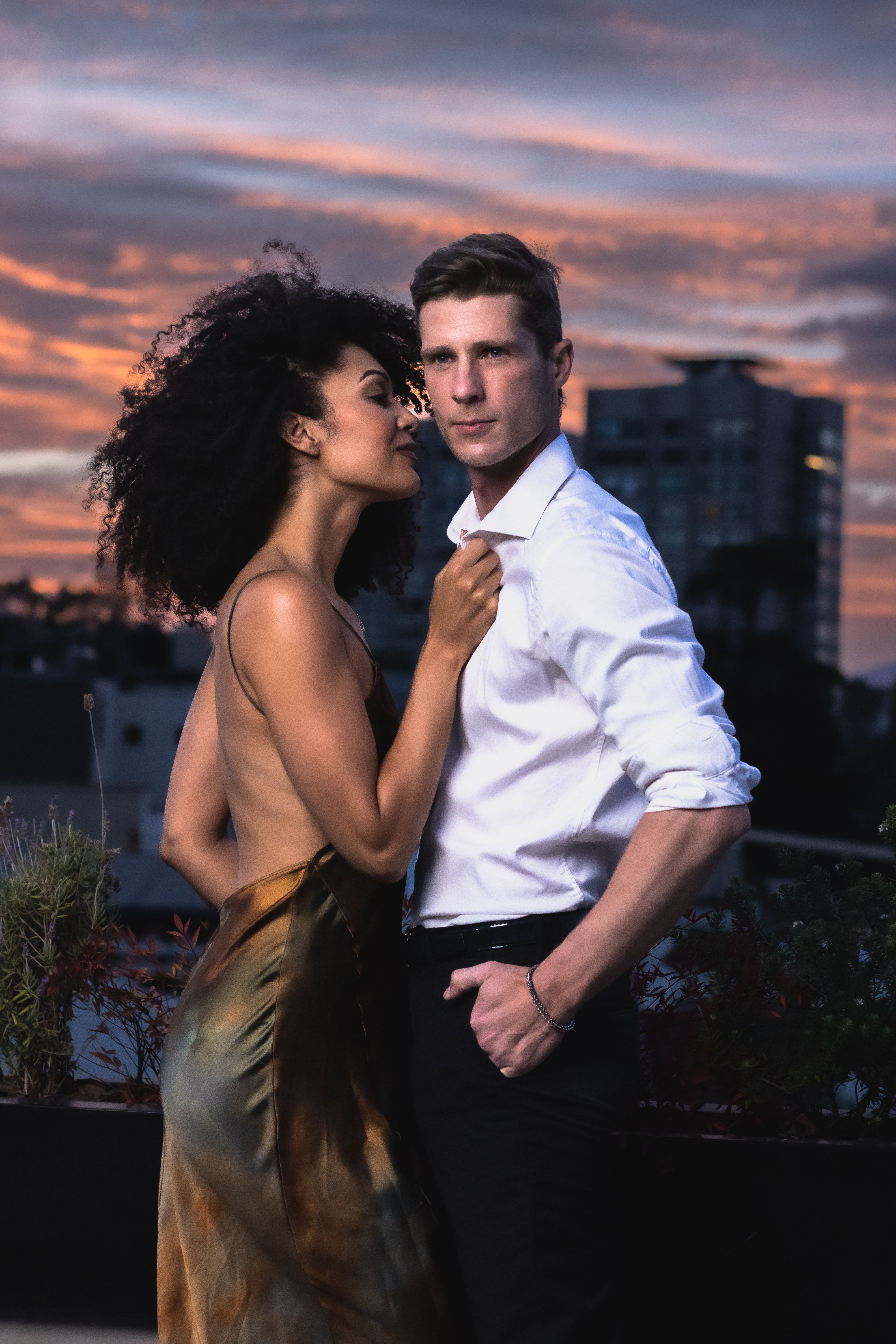 Stylish couple embracing on a rooftop at sunset, exuding romance and elegance.
