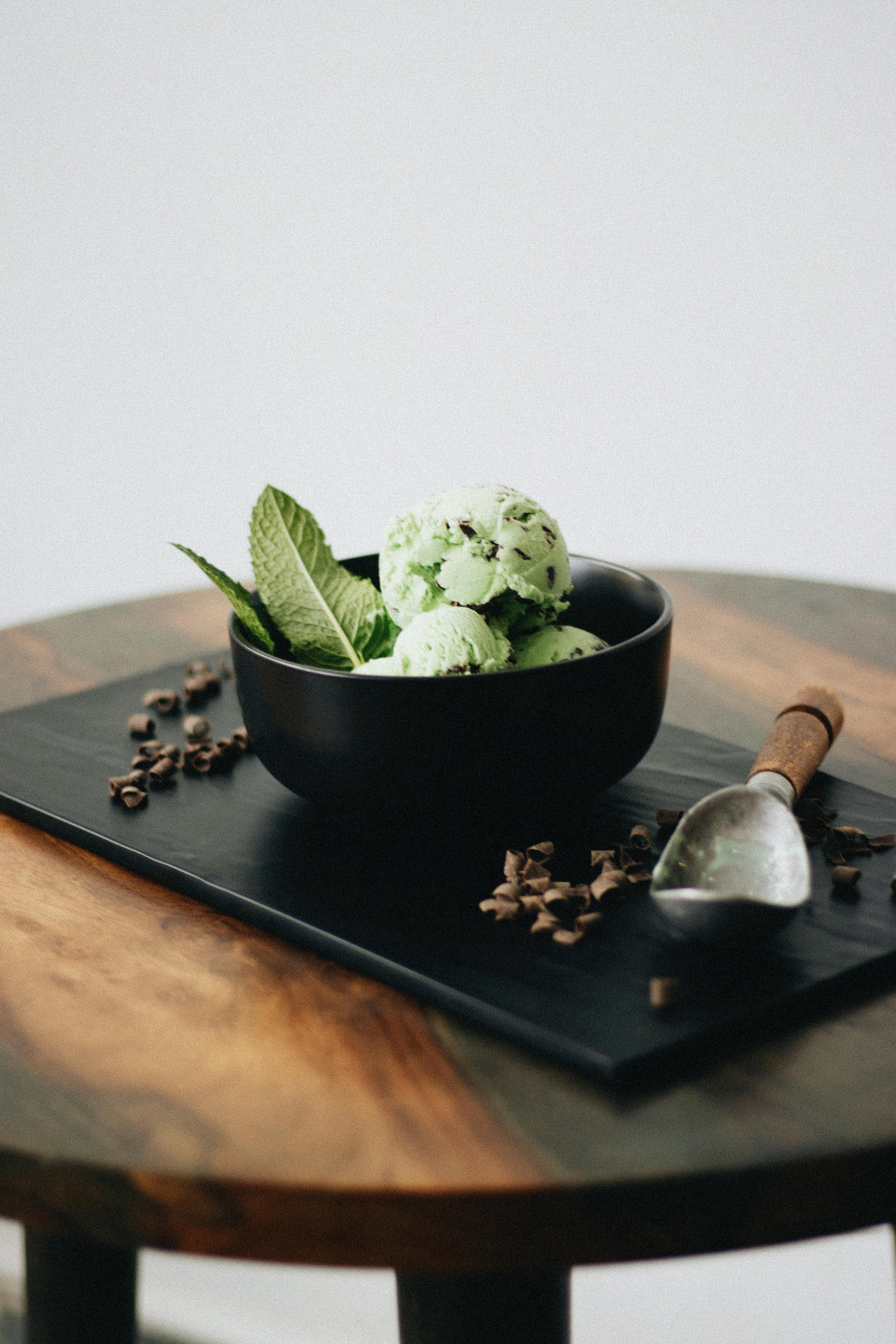 Close-up of mint chocolate chip ice cream with fresh mint leaves in a black bowl, styled elegantly.