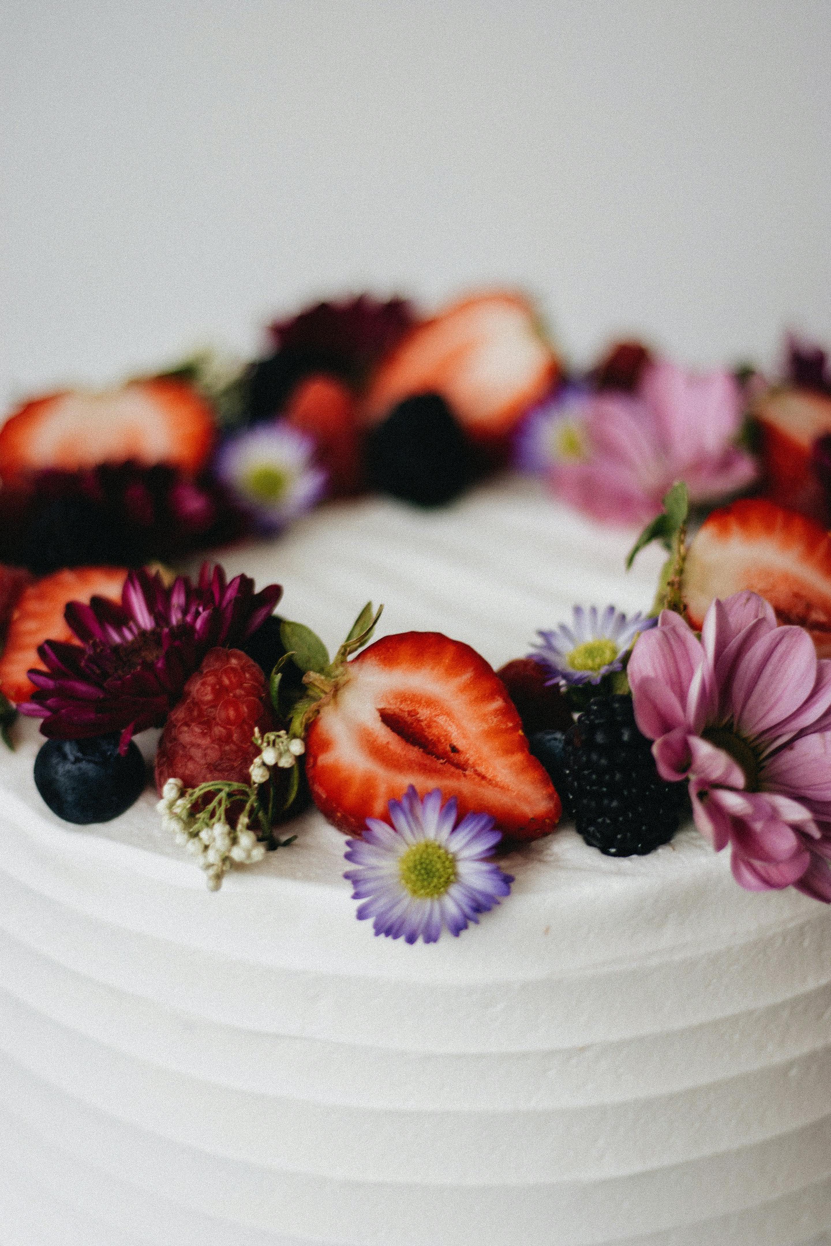 Artisanal cake adorned with fresh berries and flowers, showcasing culinary artistry.