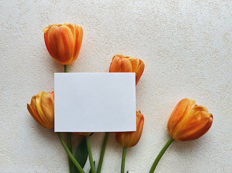 Elegant minimalist mockup with a blank card surrounded by orange tulips on a textured surface.