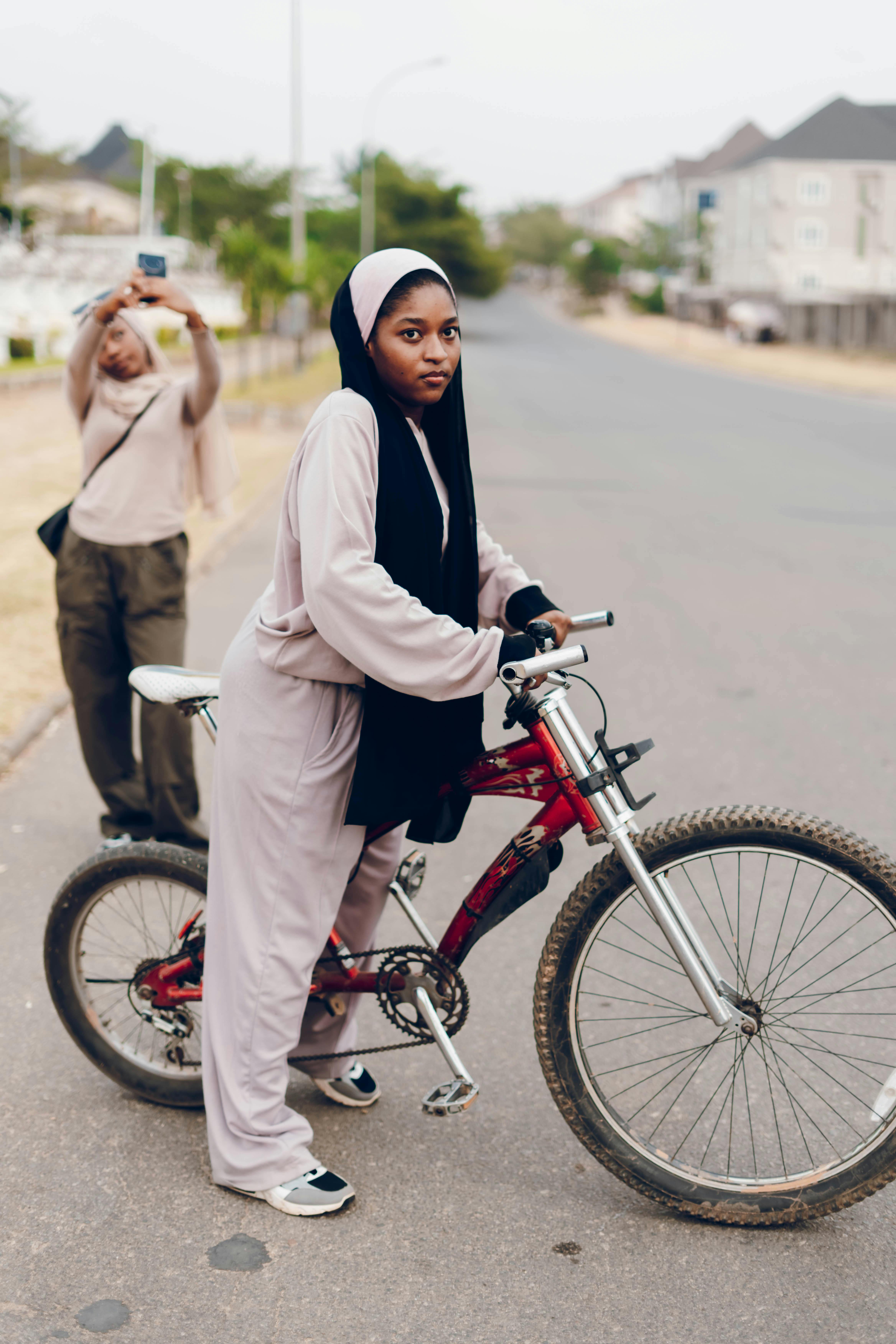 Free Young woman standing with bicycle on urban street, another taking selfie. Stock Photo