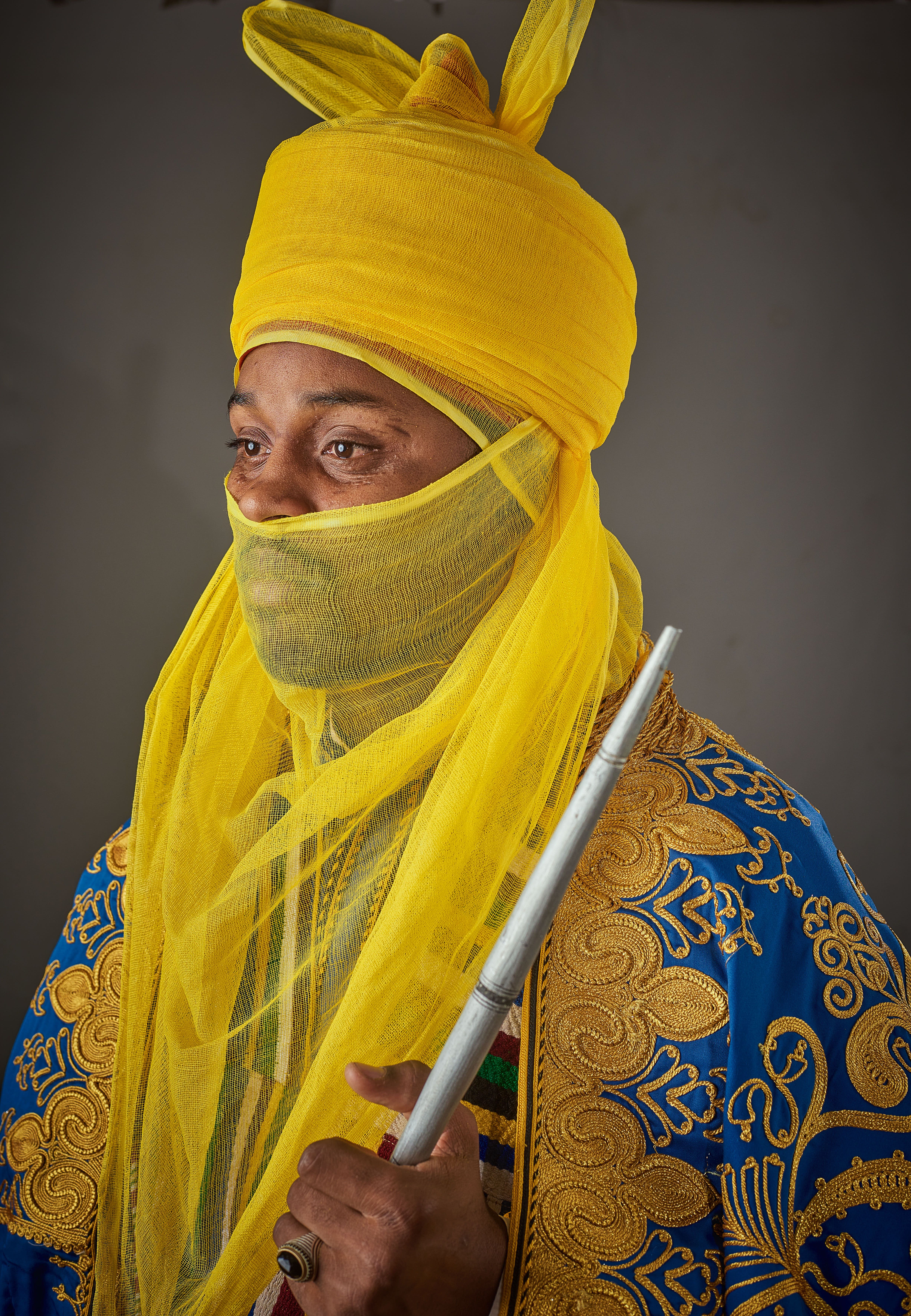 Man in vibrant traditional African attire with detailed embroidery and yellow headwrap.