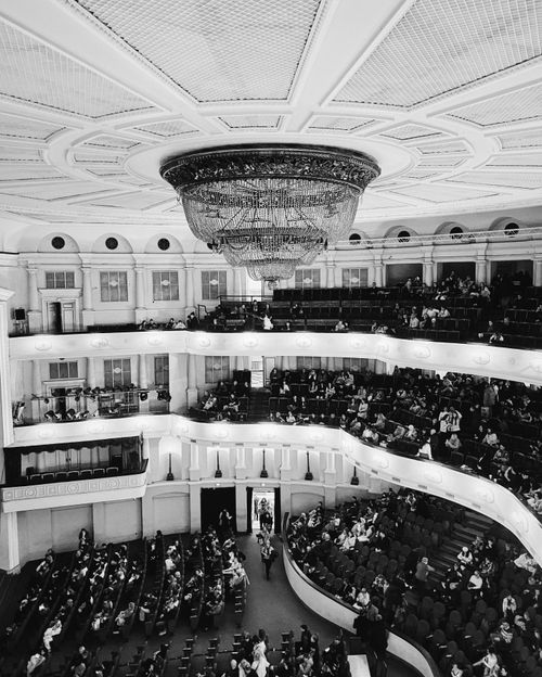Free Black and white photograph of a grand theater interior with a large chandelier and audience. Stock Photo