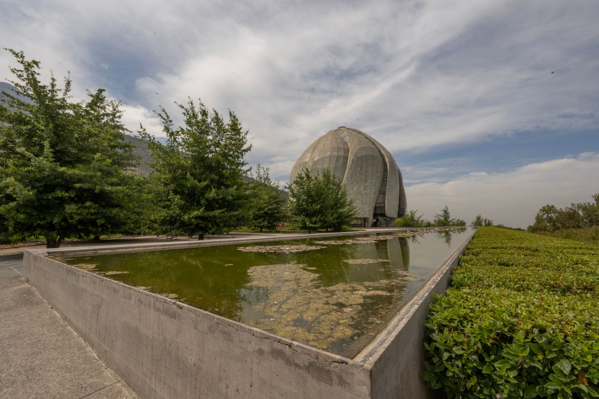 A modern temple with unique architecture reflected in a serene water feature amidst lush greenery.