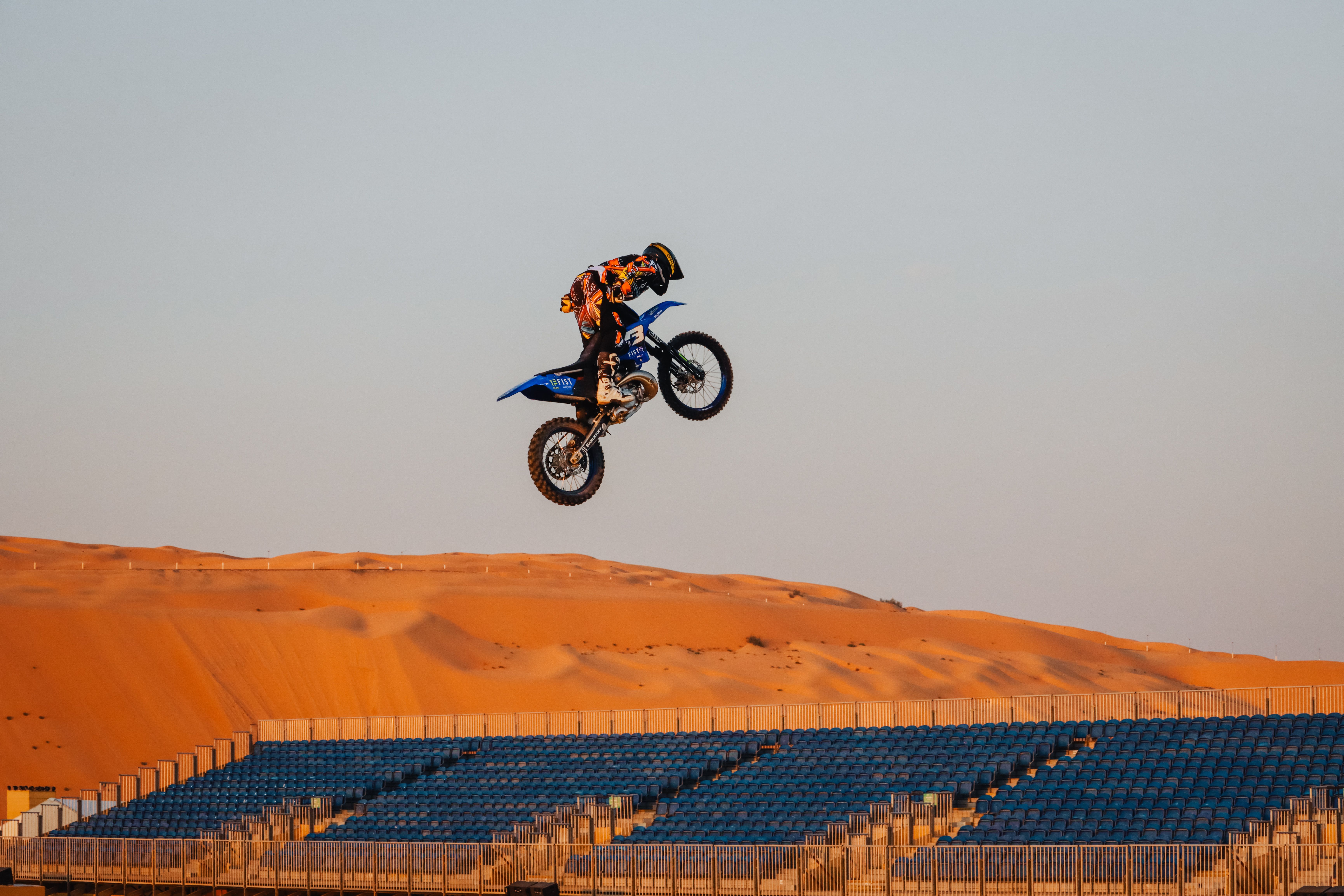 Breathtaking dirt bike aerial stunt over a desert landscape with grandstands.