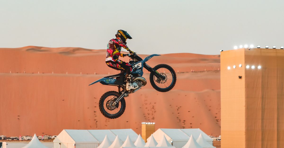 A motorbike stunt performer leaps high in Abu Dhabi's stunning desert landscape.