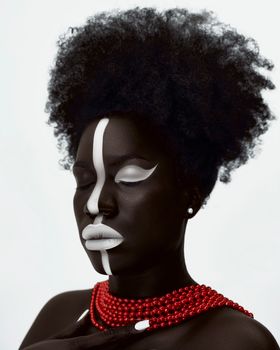 Striking artistic portrait of a woman with white face paint and red necklace against a neutral background.