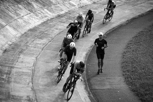 Black and white of cyclists racing on an outdoor track, with a runner alongside.