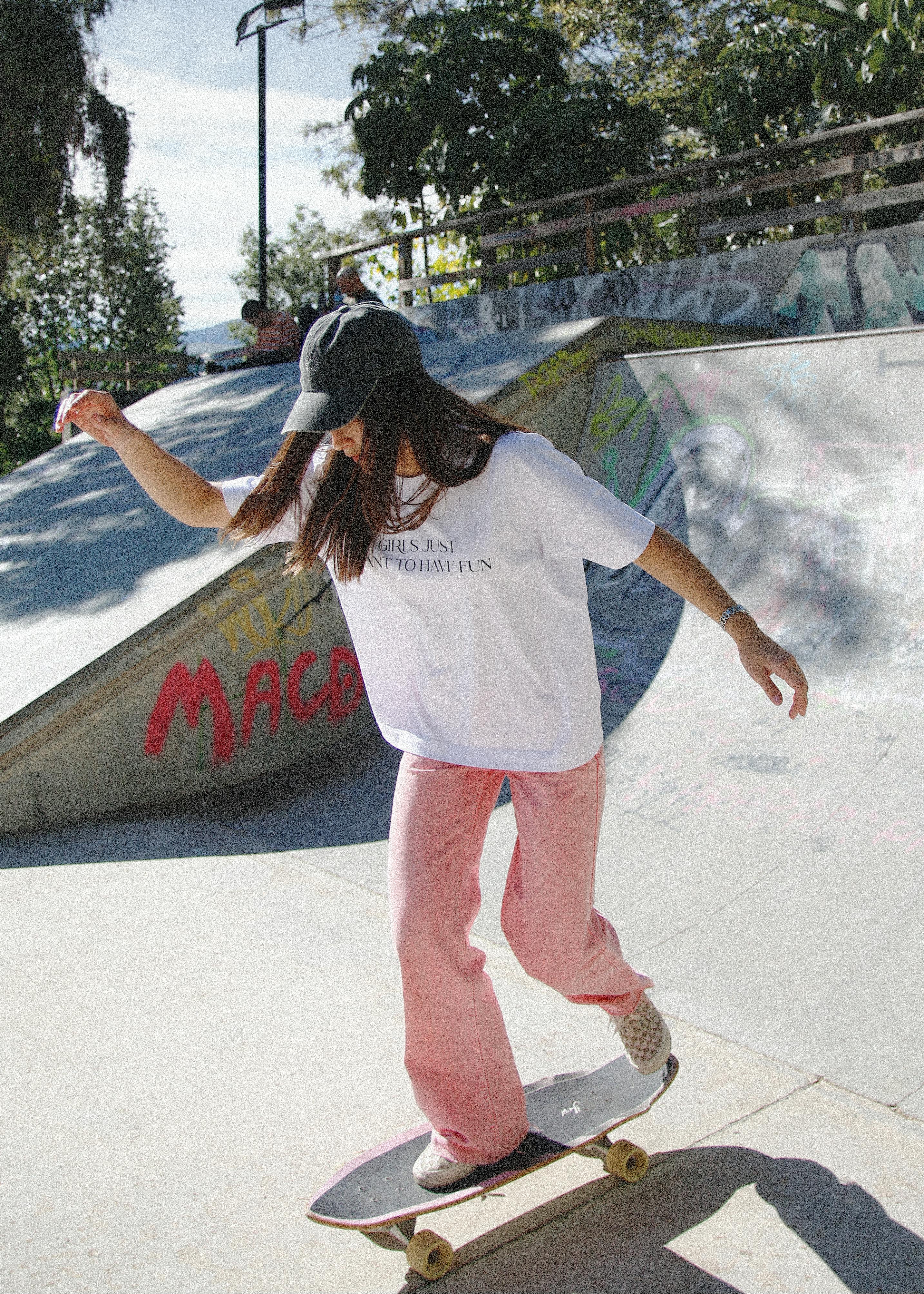 Teen girl in casual outfit skateboarding outdoors in an urban skatepark, enjoying a sunny day.