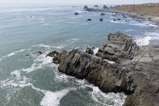 Scenic view of rugged rocky coastline with waves crashing on cliffs under a clear sky.